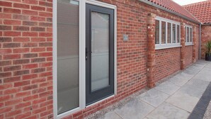 A brick building with large glass doors and windows, a tiled roof, and a paved walkway.