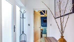 A hallway with a coat rack, a wooden table, and a vase with branches.