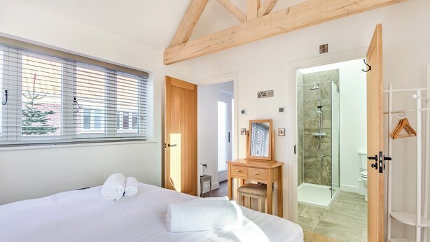 A hotel room with a large bed, a wooden dresser, a mirror, and a walk-in shower.