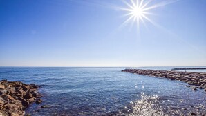 En klar, blå himmel med en strålande sol över en klippig kuststräcka.
