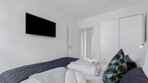 Een moderne hotelkamer met een bed, een flatscreen-tv, een kledingkast en een deur die naar een andere kamer leidt.