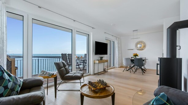 Een ruime woonkamer met balkon en uitzicht op zee, een eethoek en een open haard.