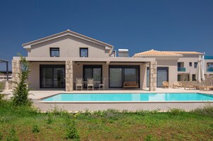 Una casa de dos pisos con piscina, pilares de piedra y un patio con mobiliario exterior.