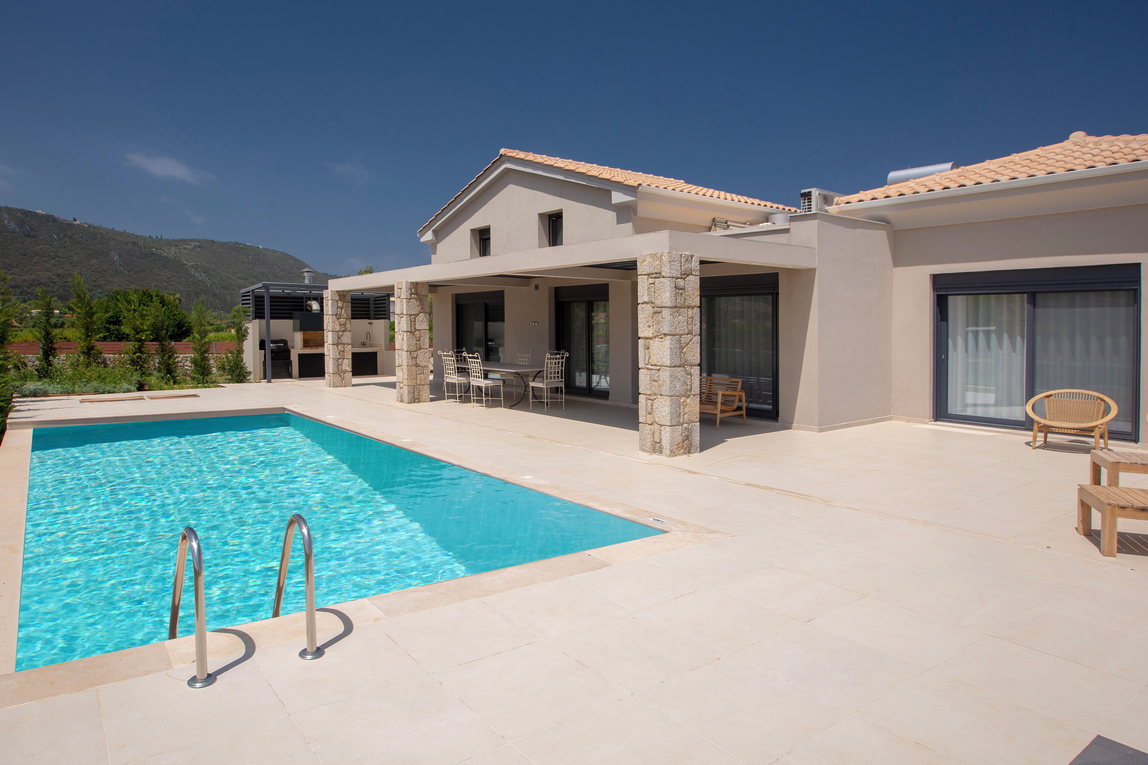 A modern house with a swimming pool, stone pillars, and a patio with outdoor furniture.