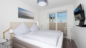 A neatly arranged bedroom with a bed, bedside lamps, a TV, and a window with a view of buildings. - Beautiful apartment in Olpenitz (Olpenitz)