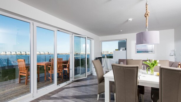 A modern dining area with a view of the sea, large sliding glass doors, and a contemporary interior design. - Beautiful apartment in Olpenitz (Olpenitz)