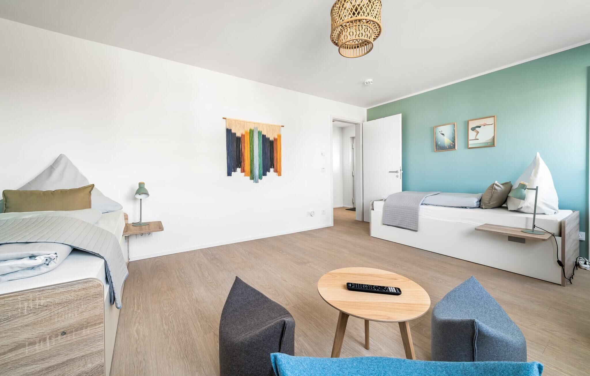 Een moderne hotelkamer met een bed, een slaapbank, een kleine tafel en een stoel. Er hangt een kunstwerk aan de muur en een deur naar een andere kamer.