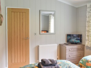 A bedroom with a wooden door, a mirror, a dresser, and a television.