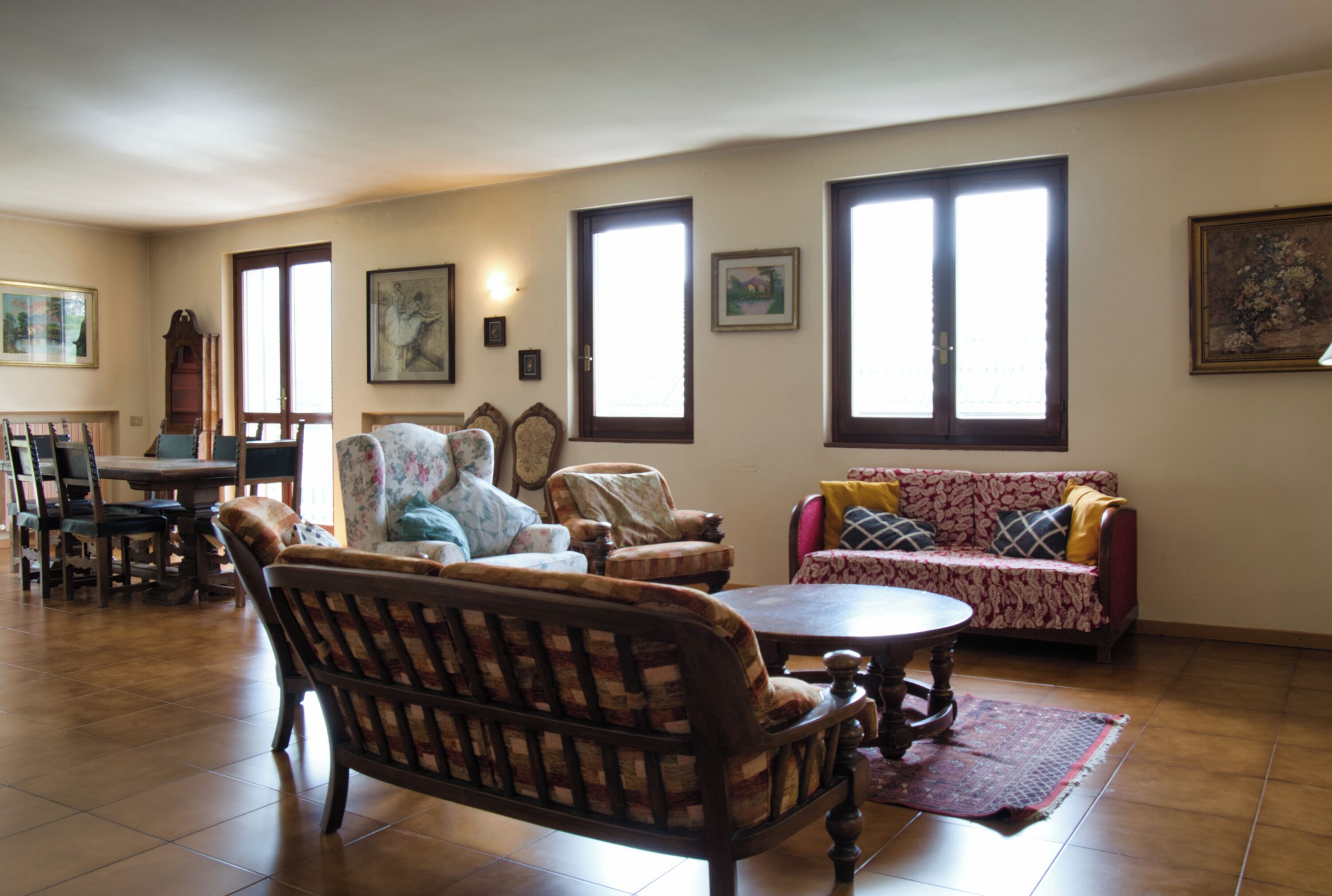 Una sala de estar con un sofá de madera, un sillón estampado, una mesa de comedor y una araña.