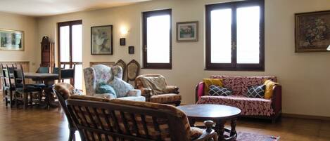 Una sala de estar con un sofá de madera, un sillón estampado, una mesa de comedor y una araña.