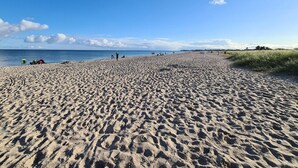 A wide sandy beach with footprints leading to the water, a clear sky, and a few people in the distance. - Lovely apartment in Olpenitz with sauna (Olpenitz)
