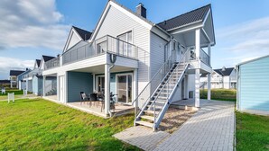 A two-story house with a balcony, a covered patio, and a staircase leading to the upper floor. - Lovely apartment in Olpenitz with sauna (Olpenitz)