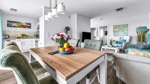 A modern living space with a wooden dining table, green upholstered chairs, a fruit bowl, and a TV in the background. - Beautiful apartment in Olpenitz (Olpenitz)