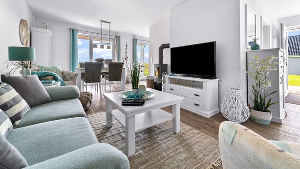 A modern living room with a white sofa, a coffee table, a flat-screen TV, and a dining area with chairs and a table. - Beautiful apartment in Olpenitz (Olpenitz)