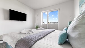A modern bedroom with a bed, a flat-screen TV, a window with a view, and a ceiling fan. - Beautiful apartment in Olpenitz (Olpenitz)