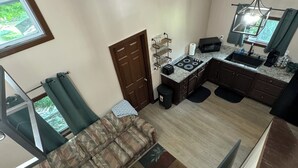 A compact living space with a sofa, a small kitchen area including a microwave and sink, and a window with curtains.