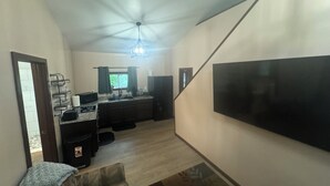 A spacious living area with a large TV, a kitchen with a sink and cabinets, and a staircase leading to another level.