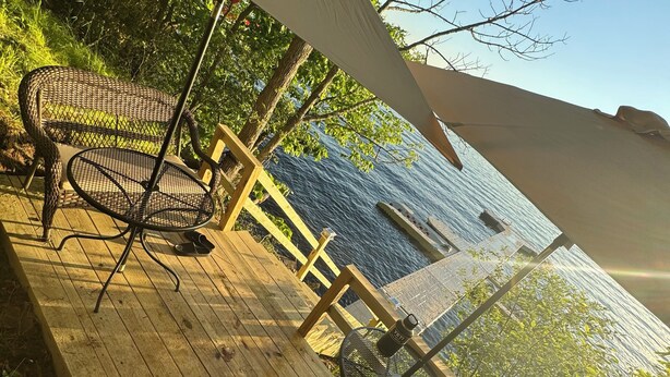 A wooden deck with wicker chairs and a table, overlooking a body of water.