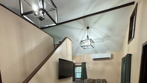 A spacious living area with a wooden floor, a sofa, a TV mounted on the wall, and a staircase.
