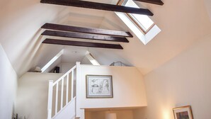 Habitación estilo loft con vigas de madera a la vista, una escalera blanca y tragaluces.