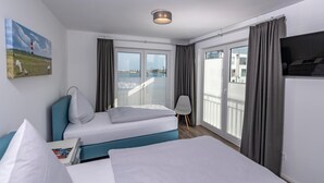 Habitación de hotel con dos camas, un cuadro, un televisor y vista al mar.