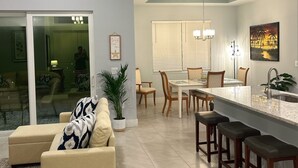 Une cuisine moderne avec un îlot central, un coin repas avec des chaises et un salon doté d’un canapé et d’une grande fenêtre.