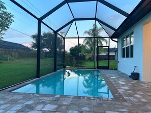 En pool utomhus med tak, med fri utsikt över trädgården, inklusive en gräsmatta och ett trästaket.