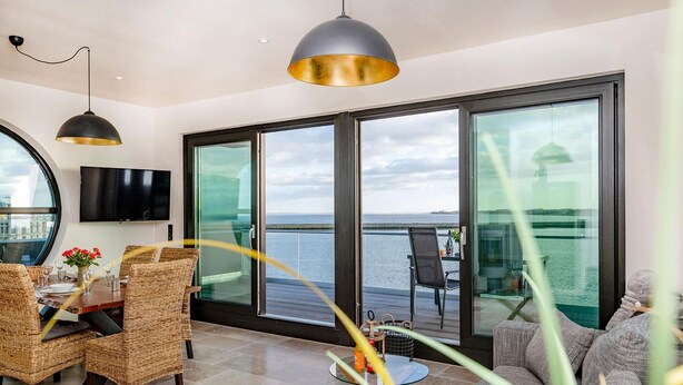 Une chambre moderne dotée d’un coin repas, d’une télévision et de grandes fenêtres donnant sur la mer.