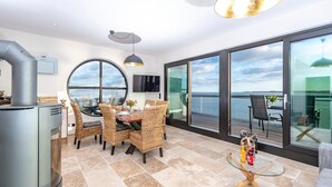 Une cuisine moderne dotée d’une cuisinière intégrée, un coin repas avec des chaises en osier, une table en verre et un balcon offrant une vue sur la mer.
