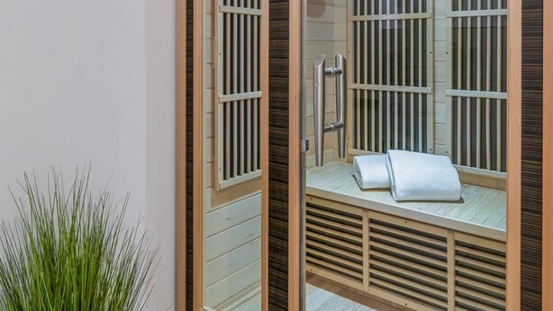 Un sauna avec des lambris en bois et une porte en verre, une serviette sur le banc et une plante en pot à côté.