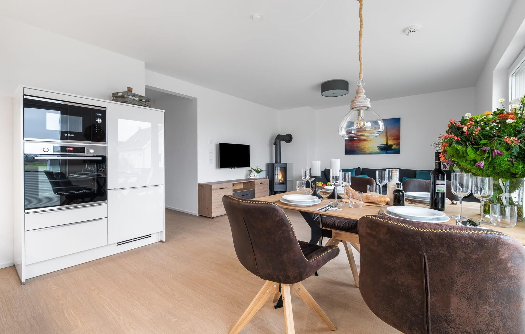 A modern kitchen with Bosch appliances, a dining area with a wooden table and leather chairs, and a large window with a view of the outdoors.