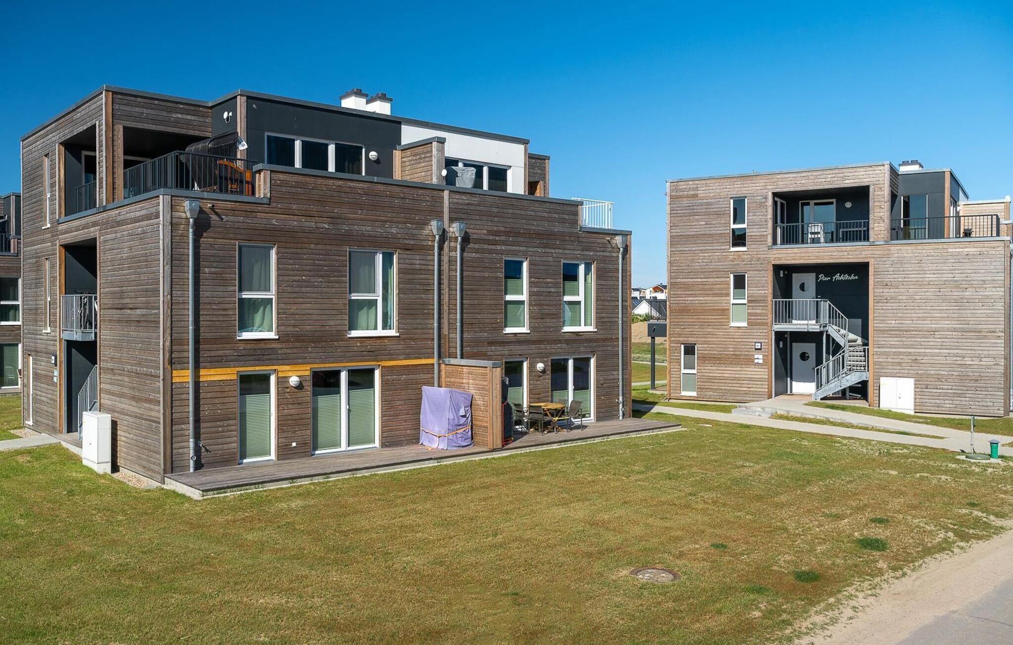 Un moderno edificio residencial de varios pisos con balcones, ventanas grandes y techo plano.