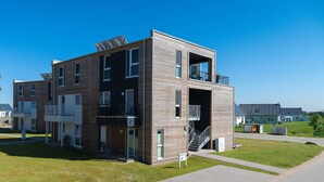 Un edificio residencial moderno de varios pisos, con balcones, un área exterior cubierta y una escalera que conduce a un piso superior.