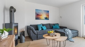 Un salon moderne avec un canapé gris, une table basse ronde en bois et un poêle à bois noir.