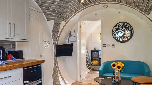 A modern kitchen with white cabinets, a black refrigerator, and a coffee machine. There is a blue sofa with a vase of sunflowers in the living area. - An amazing and extraordinary property. (Hastingleigh, near Ashford)