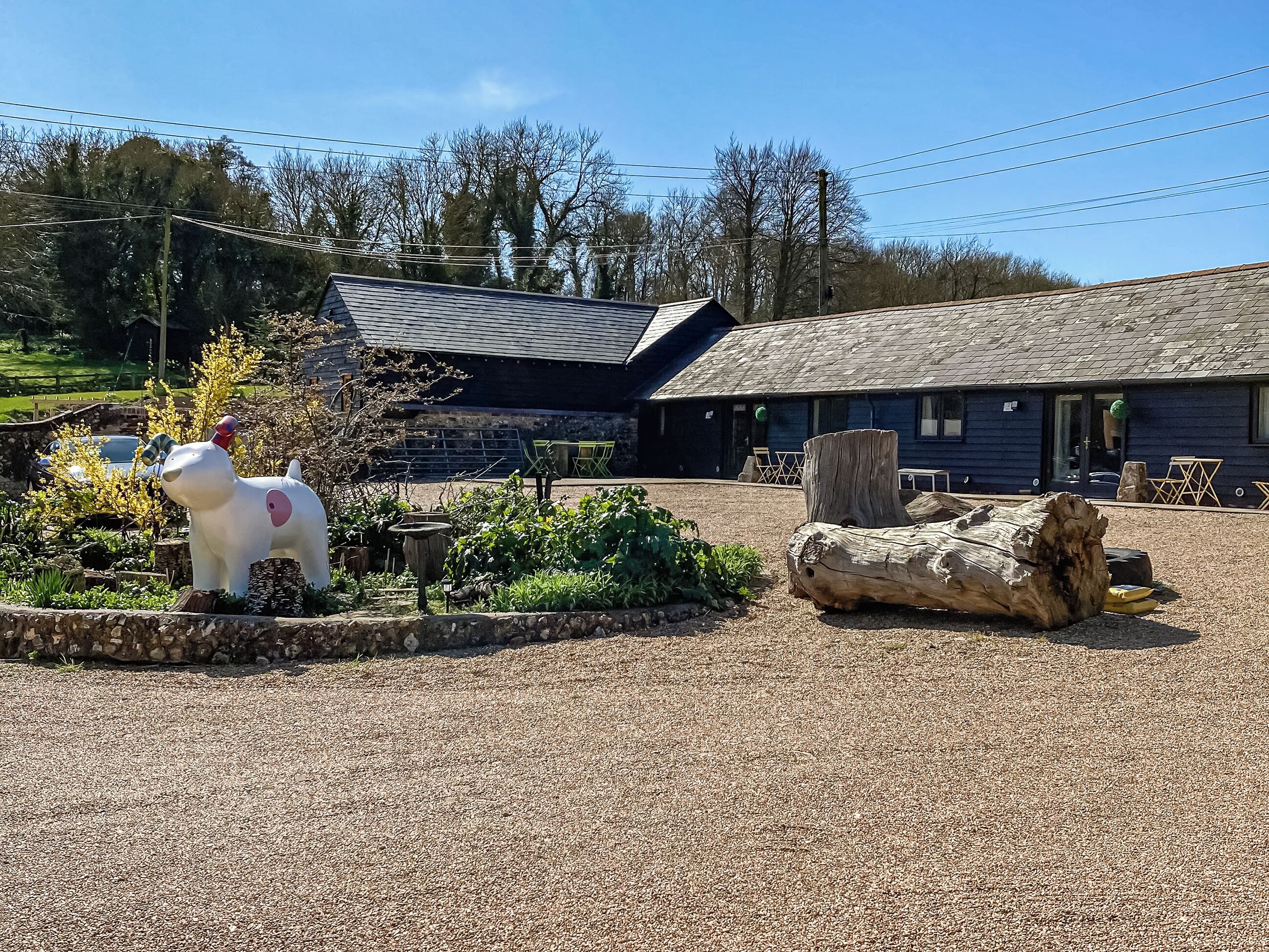 A building with a gravel driveway, a large log, and a white animal statue.
