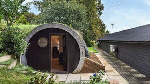 A small, circular wooden structure with a door leading into a room, surrounded by a garden and a pathway. - An amazing and extraordinary property. (Hastingleigh, near Ashford)