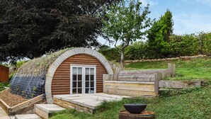 A small wooden structure with a sloped roof, a wooden bench, and a metal pot on a stand. - An amazing and extraordinary property. (Hastingleigh, near Ashford)