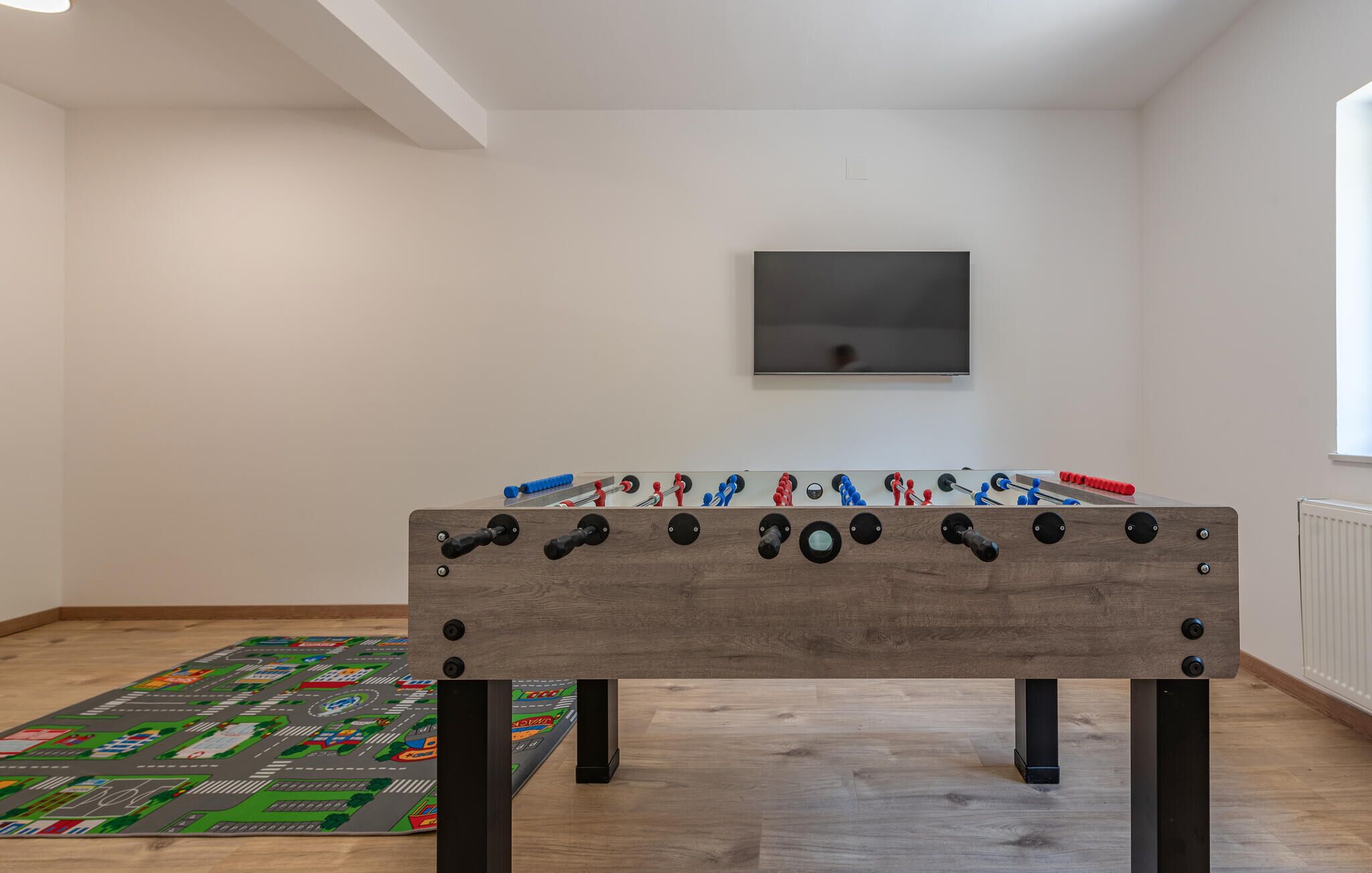 Ein Zimmer mit einem Holztischfußball, einem an der Wand montierten Fernseher und einem bunten Brettspiel auf dem Boden.