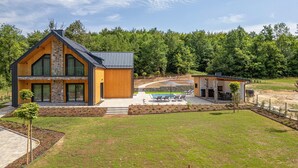 Una moderna casa a due piani con facciata in pietra, ampie finestre e un giardino curato con piscina e area salotto all'aperto.