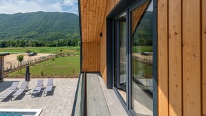 Un edificio moderno con rivestimento in legno e ampie finestre. Dispone di una zona piscina con lettini e vista su un paesaggio verde e montagne sullo sfondo.