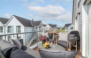 Un balcon agrémenté de mobilier d’extérieur, une table à manger ornée d’un vase de fleurs et une vue sur les maisons voisines.