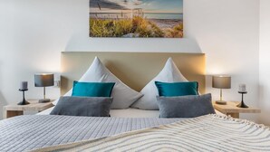 A bedroom with a bed, two nightstands, a lamp on each, and a painting of a beach scene above the bed. - Beautiful apartment in Olpenitz (Olpenitz)