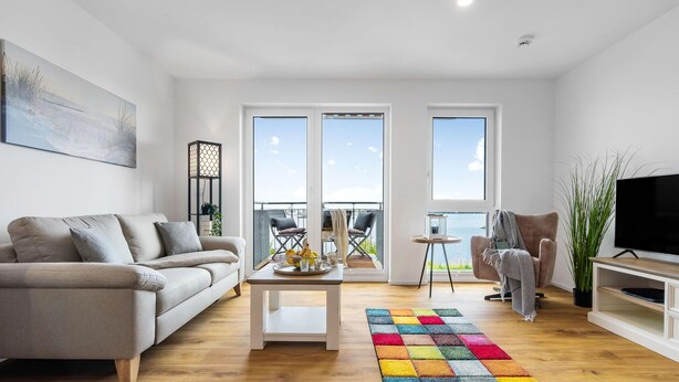 A modern living room with a sofa, a coffee table, a colorful rug, a TV, and a balcony with a view. - Beautiful apartment in Olpenitz (Olpenitz)