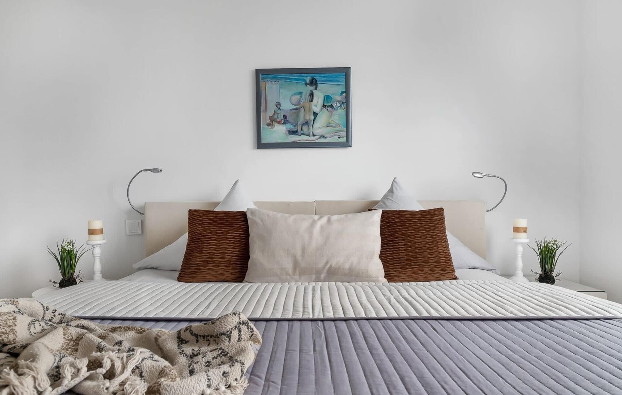 Una camera da letto ordinata con un letto, cuscini, un comodino con una candela e un quadro appeso al muro.