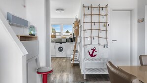 A modern kitchen with a view to the outdoors, a washing machine, and a red stool.
