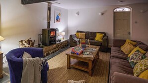 A cozy living room with a fireplace, a blue armchair, a brown sofa, and a coffee table with board games. - Chapel Cottage - UKC4683 (Clynnog Fawr)