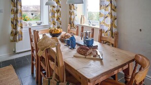 A wooden dining table with chairs, a bowl of fruit, blue cups, and a loaf of bread. - Chapel Cottage - UKC4683 (Clynnog Fawr)