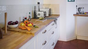 A kitchen with white cabinets, a wooden countertop, a bowl of vegetables, a toaster, and a kettle. - Chapel Cottage - UKC4683 (Clynnog Fawr)