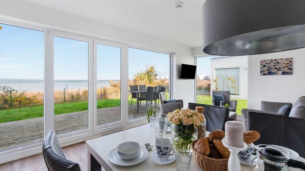 Ein Essbereich mit Blick auf das Meer, ein Tisch gedeckt mit Tellern, Tassen und einer Blumenvase.
